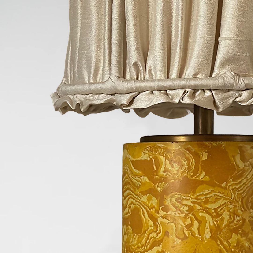 A gold marbled base table lamp with brass detailing, topped with a gold pleated shade,  available  to buy on the-salon.com. SALON curates the finest , unique, handmade pieces from the interior industry's best makers and brands. Shop luxury furniture, lighting, rugs, art, antiques and vintage pieces and accessories from SALON interior designed rooms.