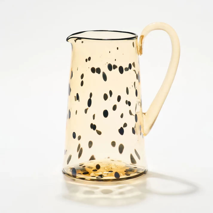 A handblown glass jug with a beige color and black dotted pattern, with a handle on the side, available  to buy on the-salon.com. SALON curates the finest , unique, handmade pieces from the interior industry's best makers and brands. Shop luxury furniture, lighting, rugs, art, antiques and vintage pieces and accessories from SALON interior designed rooms.