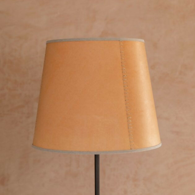 A tapered lampshade with a hand-stitched design, in Pompeian Buff colour, displayed on a stand against a neutral background, available  to buy on the-salon.com. SALON curates the finest , unique, handmade pieces from the interior industry's best makers and brands. Shop luxury furniture, lighting, rugs, art, antiques and vintage pieces and accessories from SALON interior designed rooms.