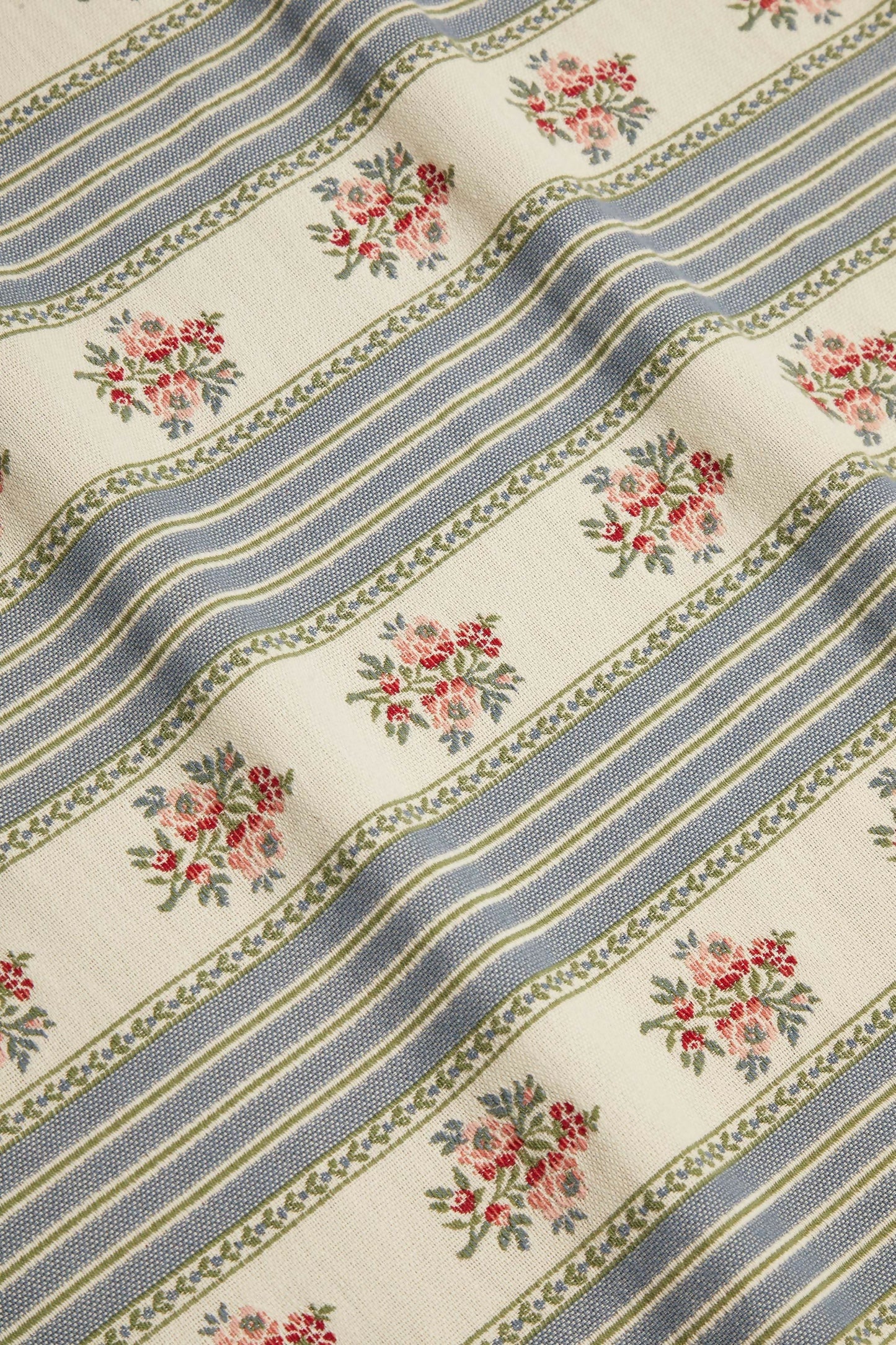 Close-up view of a fabric featuring a jacquard weave with a pattern of delicate embroidered floral motifs, stripes, and leaves in blue, green, and beige colours,  available  to buy on the-salon.com. SALON curates the finest , unique, handmade pieces from the interior industry's best makers and brands. Shop luxury furniture, lighting, rugs, art, antiques and vintage pieces and accessories from SALON interior designed rooms.