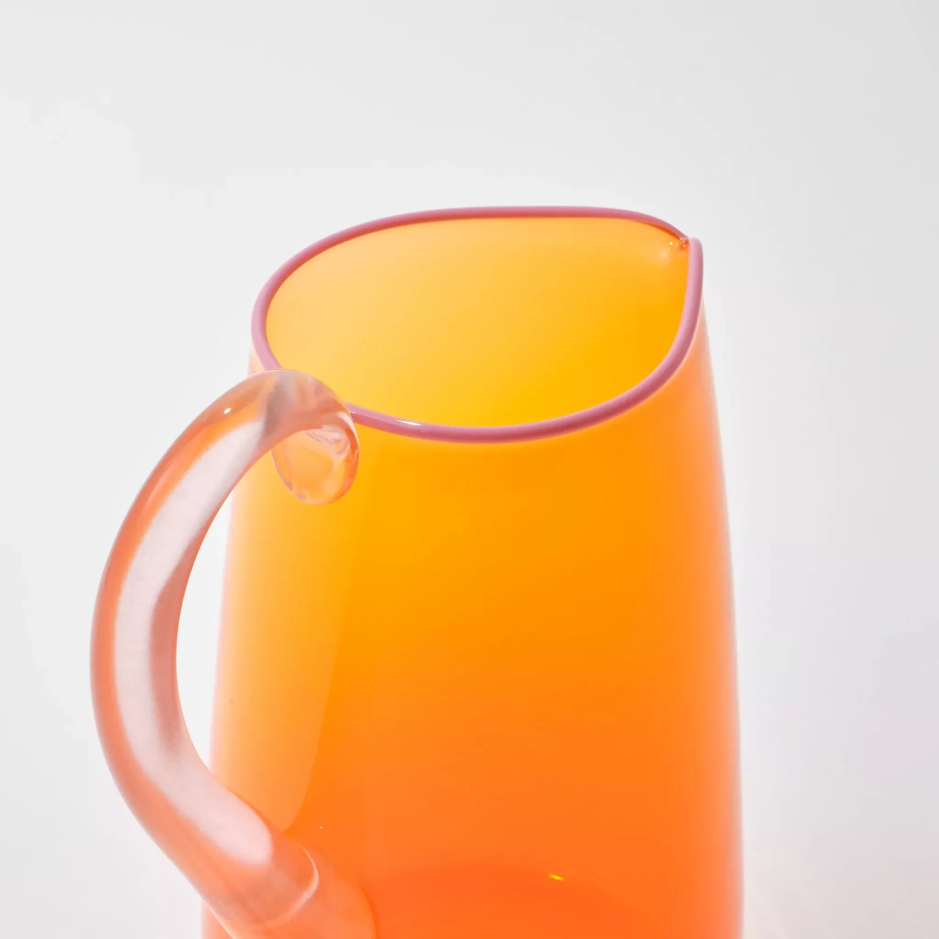 Hand blown, transparent orange glass jug with a blush handle and contrasting pale pink lip on a white background,  available  to buy on the-salon.com. SALON curates the finest , unique, handmade pieces from the interior industry's best makers and brands. Shop luxury furniture, lighting, rugs, art, antiques and vintage pieces and accessories from SALON interior designed rooms.